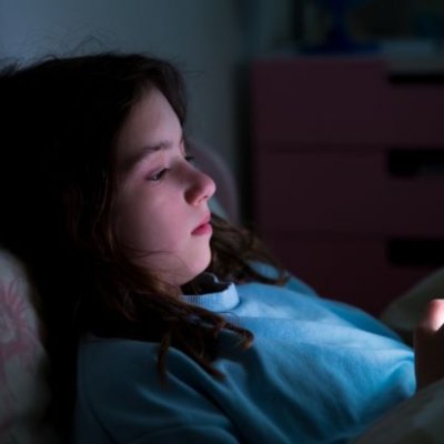 a girl's face is illuminated by the light of a phone screen